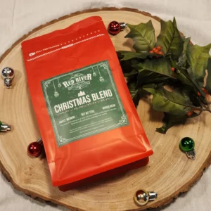 A red bag of Christmas Blend coffee from Red River Roastery with tree ornaments and holly.