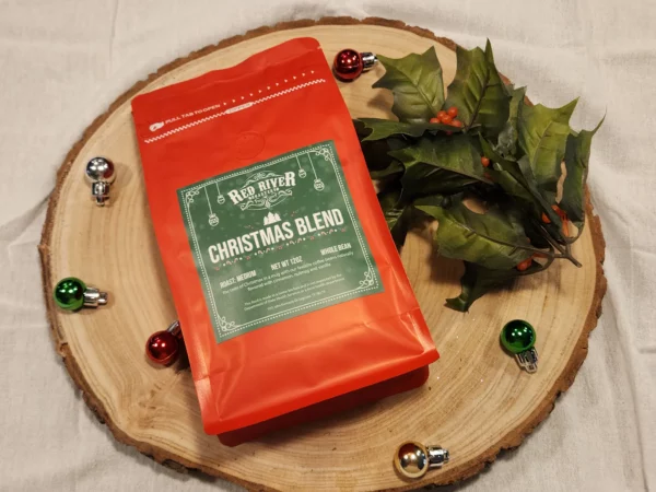 A red bag of Christmas Blend coffee from Red River Roastery with tree ornaments and holly.