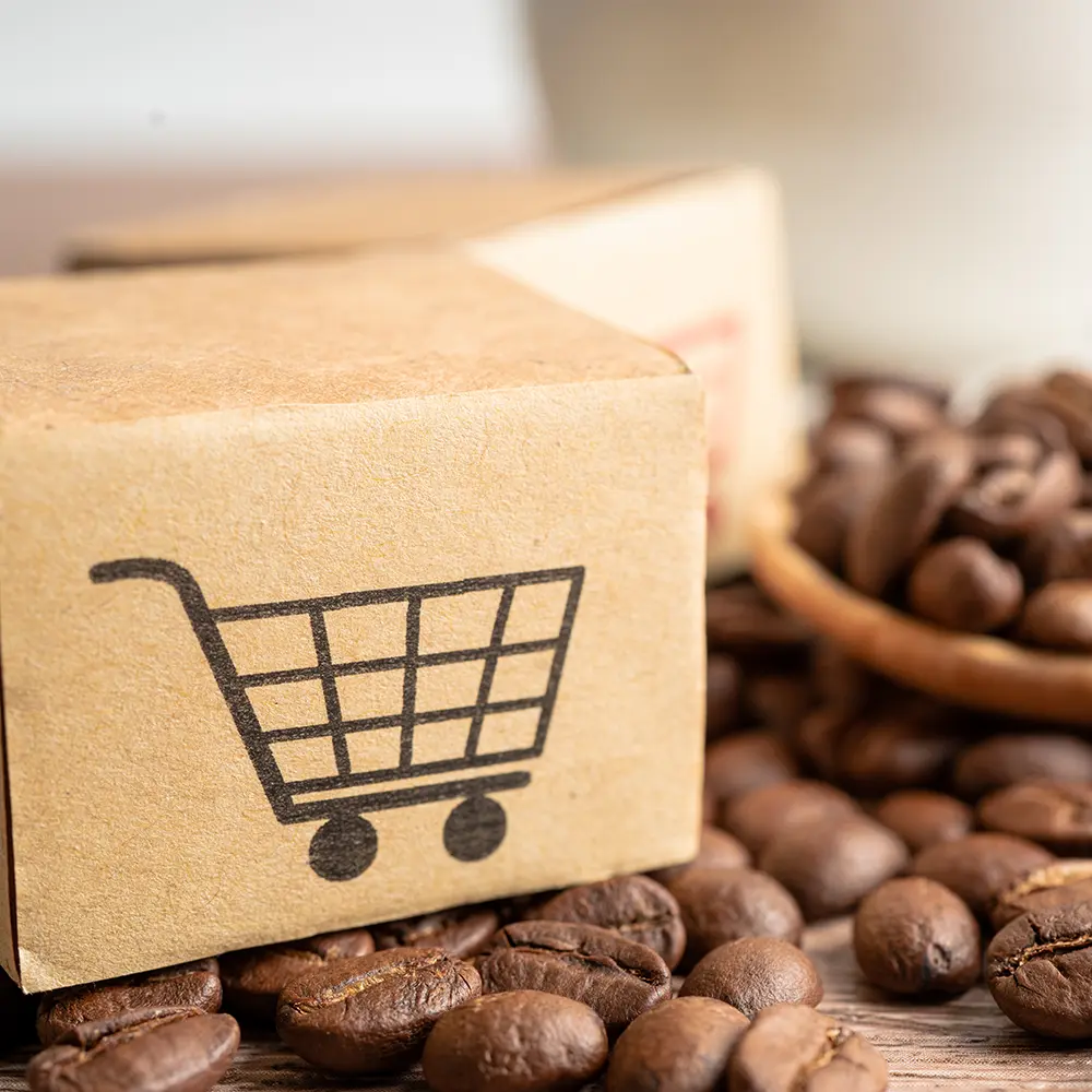 Cardboard box with shopping cart to symbolize shipping and coffee beans on a table.