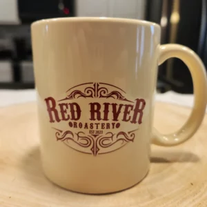 Cream colored coffee mug with maroon Red River Roastery logo.