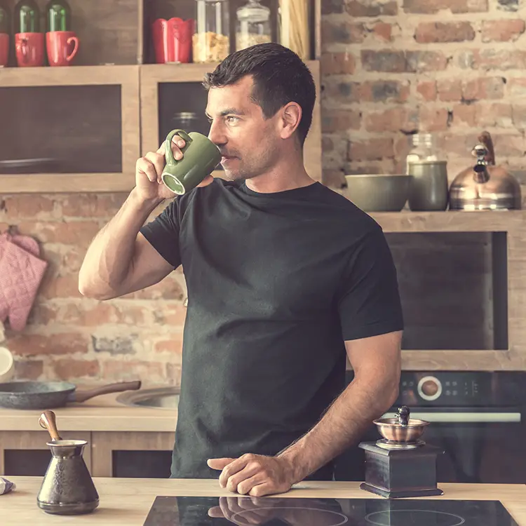 a man drinking coffee from a green mug in a kitchen